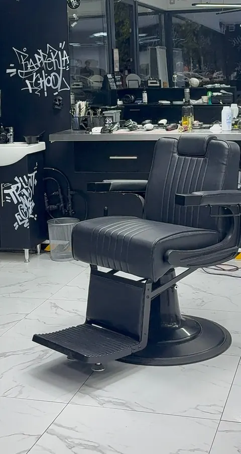 Scaunul de frizerie negru din salon, în fața oglinzii, pe podeaua de marmură.