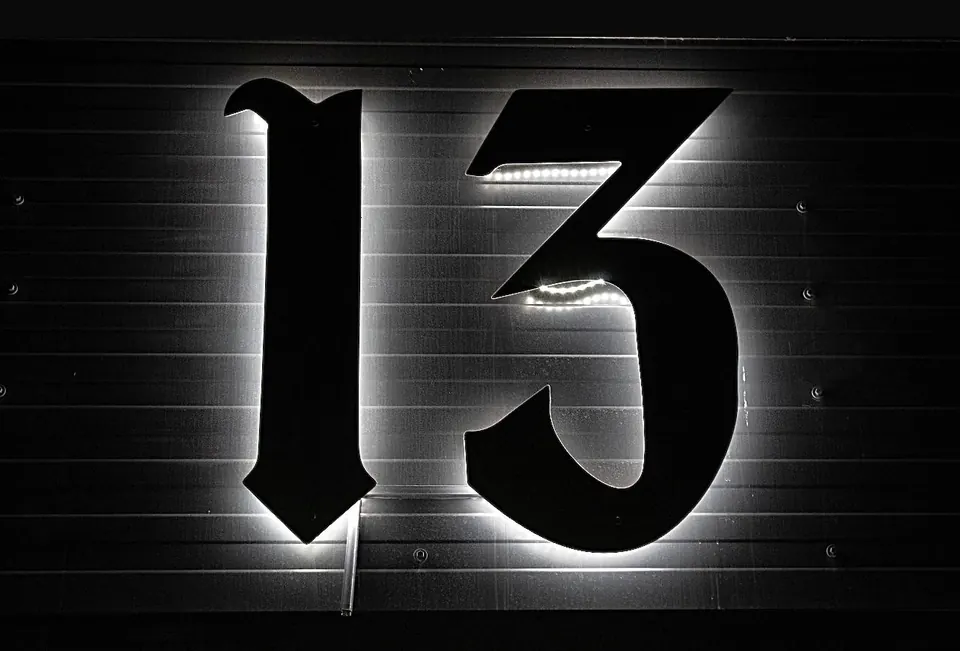 Firma 13 Barbershop noaptea: cifrele 13 negre, luminate din spate cu LED alb, pe un perete de tablă.